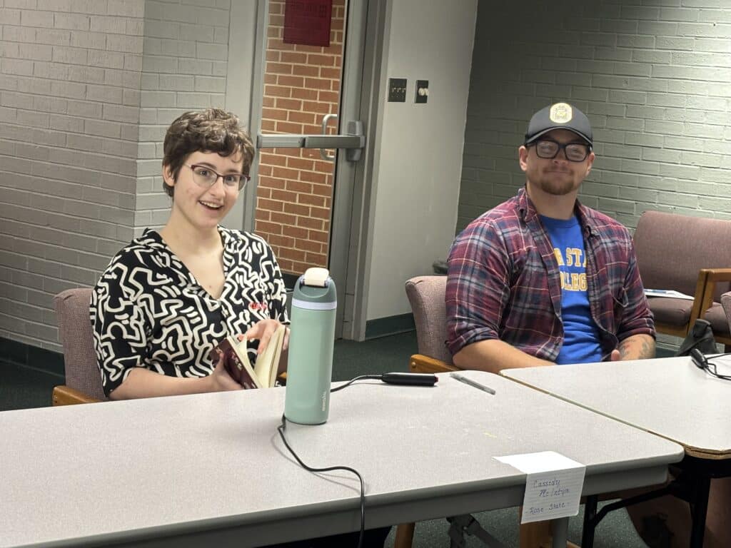 One female RSC student and one male RSC student sit at a table ready for the Quiz Bowl competition.