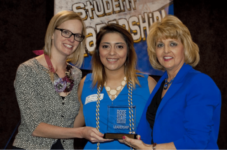 Three women pose together at a student leadership event, smiling and holding a Rose State College leadership award plaque.
