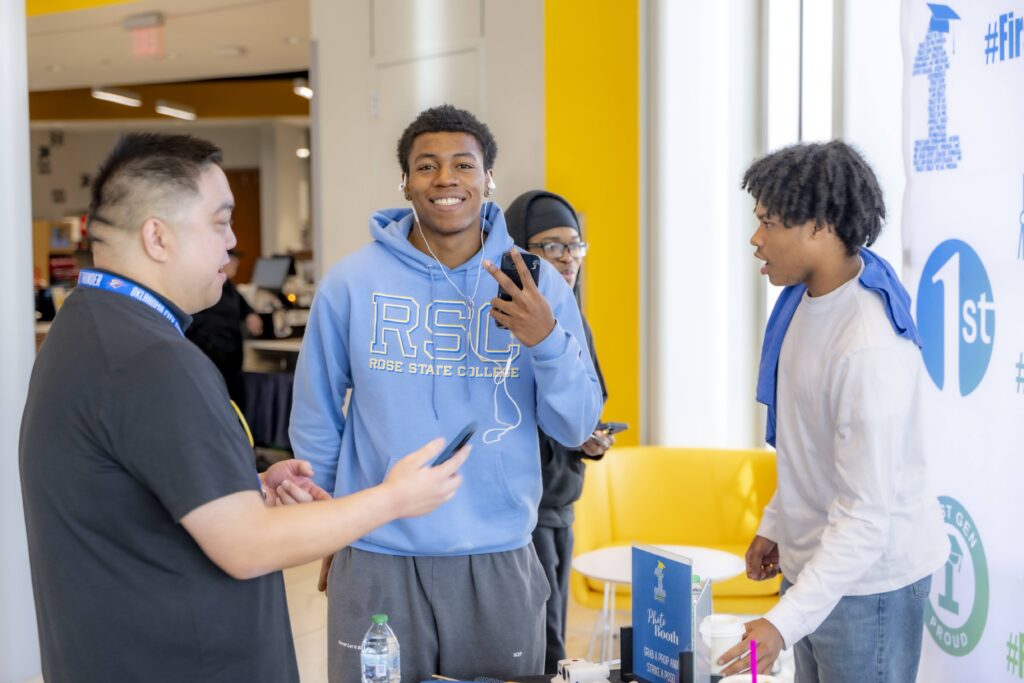 Rose State College students gather at a First Gen information table, with one student in an RSC hoodie smiling and holding up a peace sign.