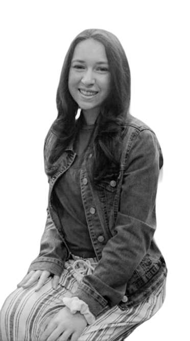 Black-and-white portrait of a smiling woman seated in a chair, wearing a denim jacket and striped pants, with long hair down.