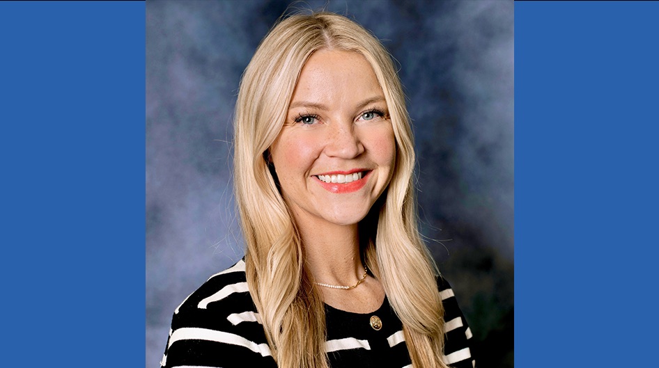 Headshot of a woman with long blonde hair smiling, wearing a black and white striped top against a studio background.
