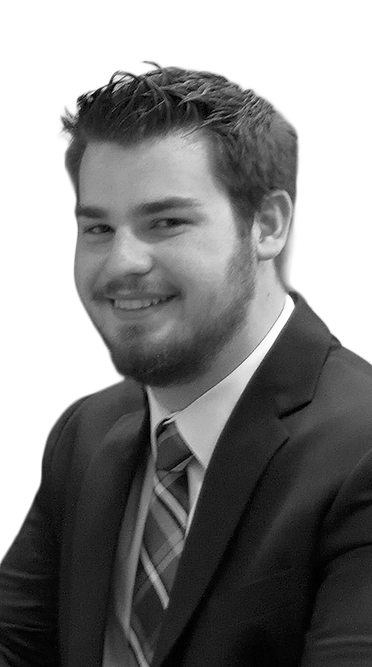 Black-and-white portrait of a smiling man with short hair and a beard wearing a suit and striped tie, seated at an event.