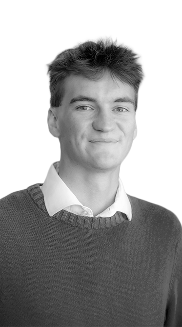 Head-and-shoulders portrait of a smiling Rose State College student wearing a white collared shirt and dark sweater, standing in front of a softly blurred wall.