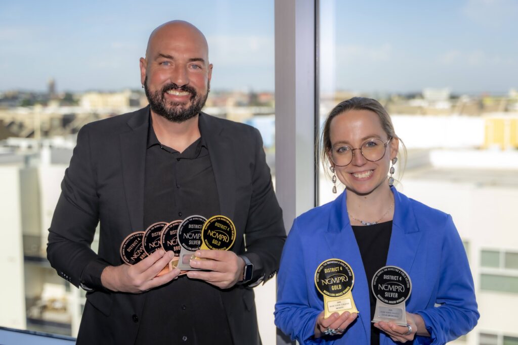 Two Rose State College Marketing and Communications team members smile while holding six NCMPR District 4 awards, including gold, silver, and bronze honors, at the regional conference.